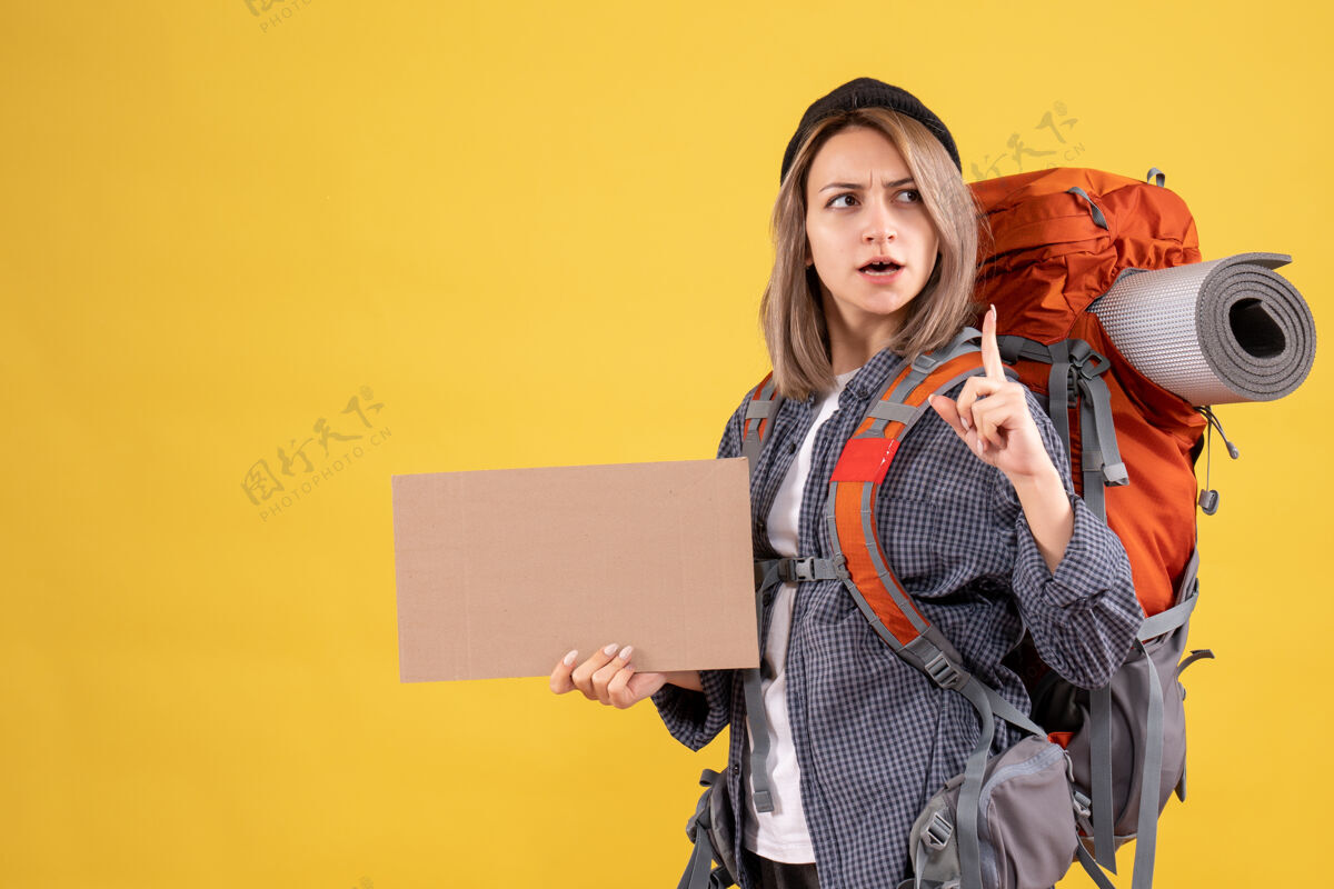 纸板一个背着背包拿着纸板的女旅行者 手指朝上女旅客手指指着