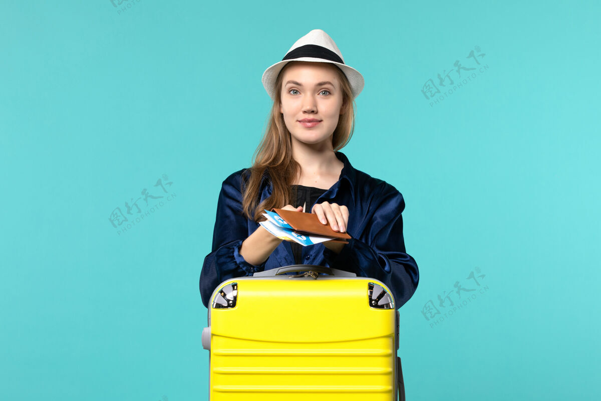 微笑前视图年轻女子拿着她的机票 准备乘坐蓝色背景的旅行飞机出海度假旅行举行航行准备