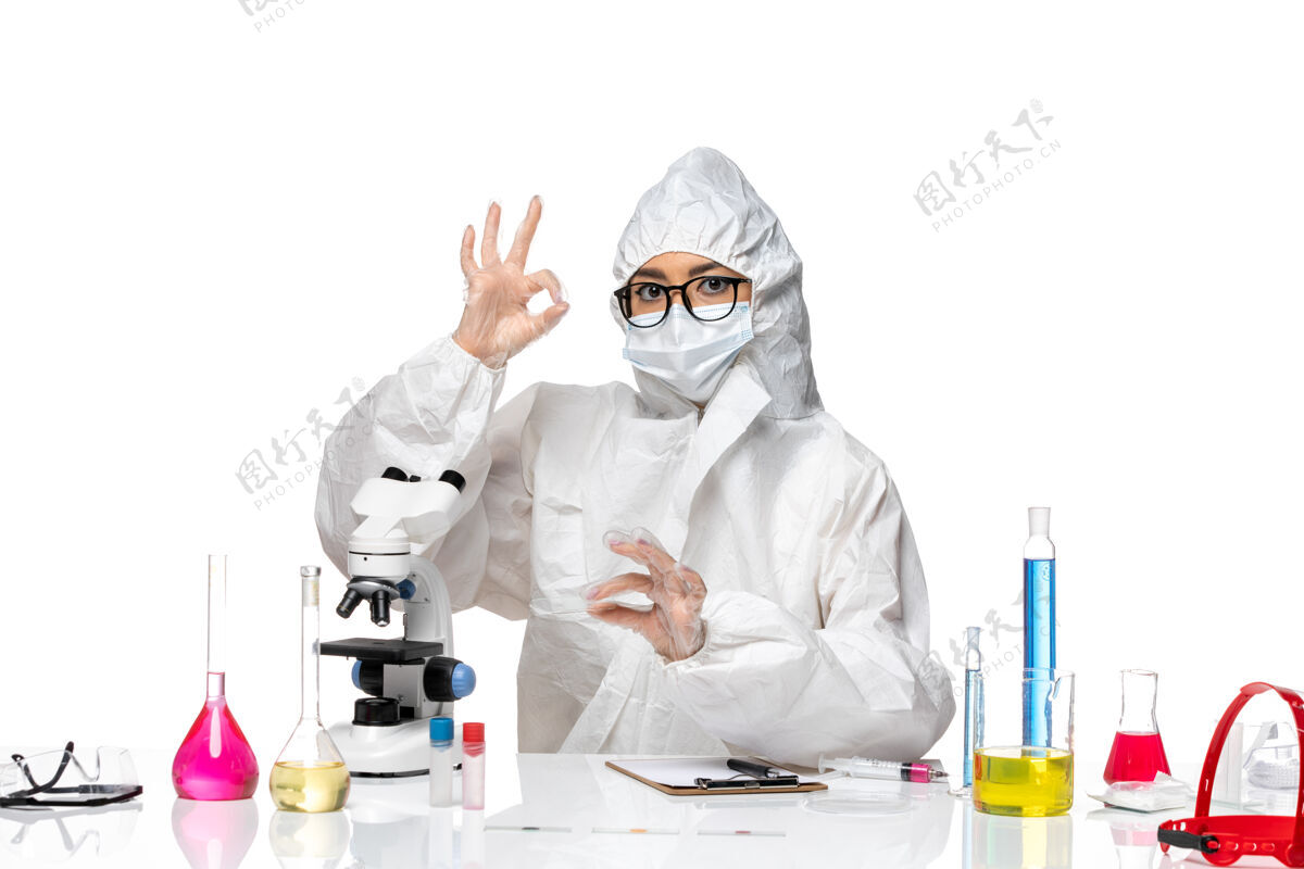 套装正面图身着特殊防护服的年轻女化学家在白桌病毒实验室用显微镜工作-健康化学实验室外套防护病毒