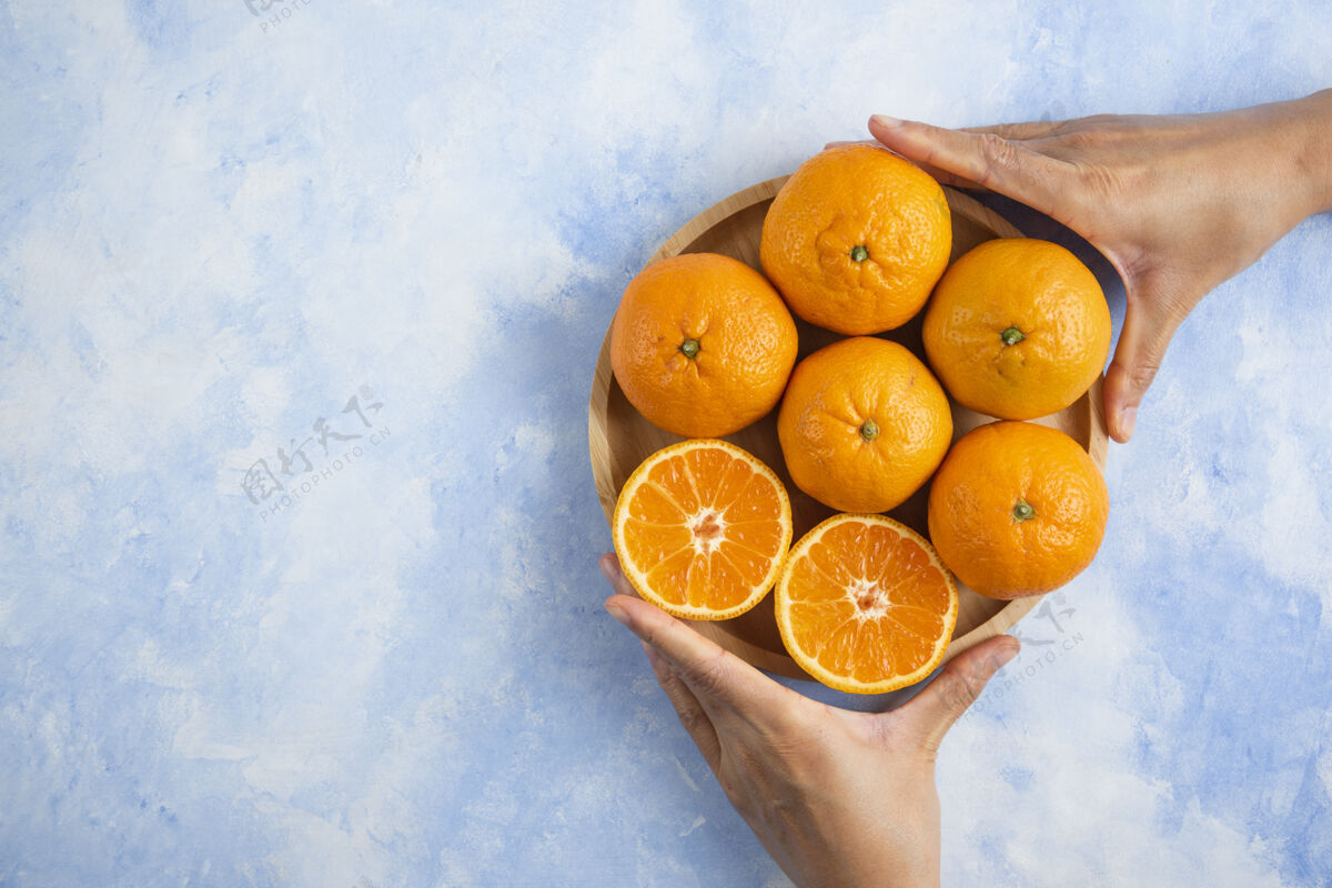 柑橘女性手拿着从堆里切下来的切片蓝色表面上的蜜柑自然堆美味