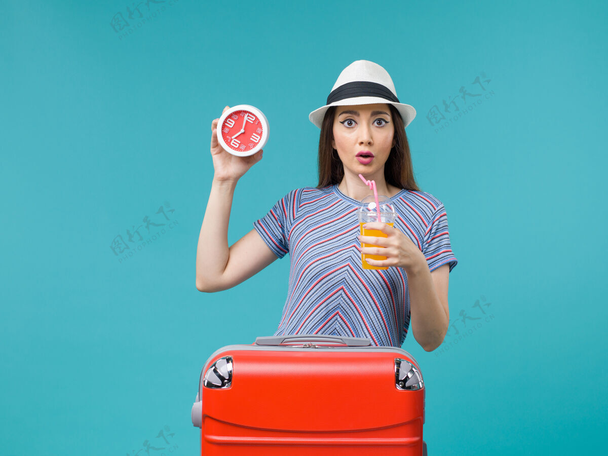 男性前景：度假中的女人拿着果汁和闹钟在蓝色的背景上航行度假海上旅行微笑人旅行