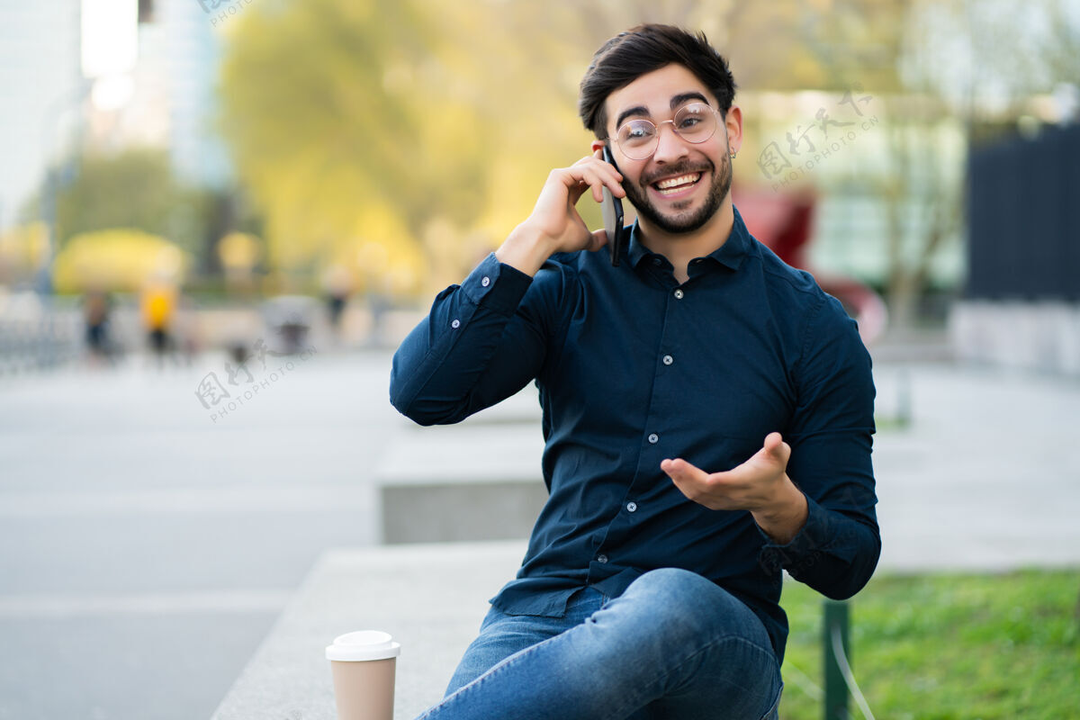 男人坐在户外长凳上打电话的年轻人的画像城市概念正面电话户外