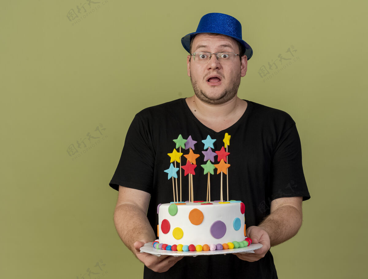 举行令人印象深刻的成年斯拉夫人戴着眼镜戴着蓝色派对帽拿着生日蛋糕橄榄色印象穿