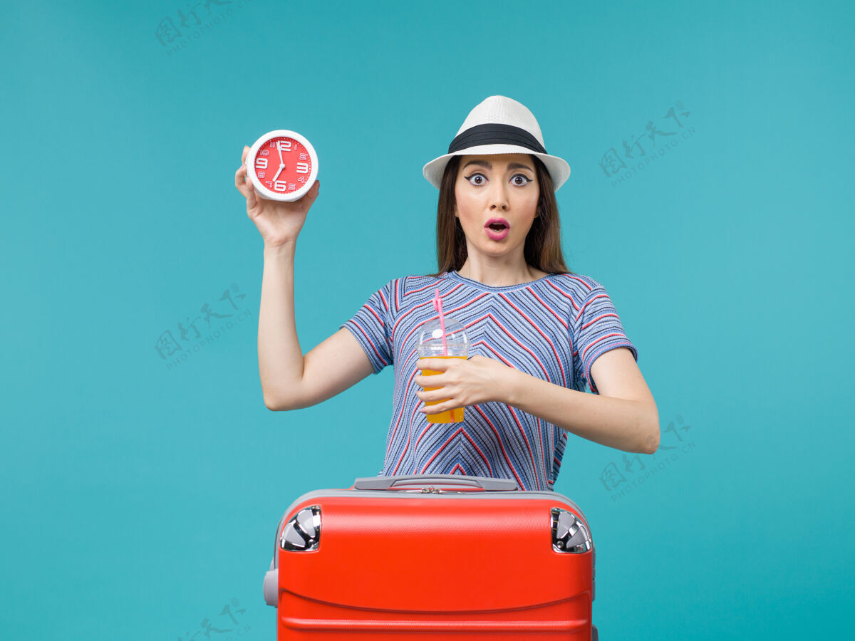 运动装前景度假中的女人手持果汁和钟表在淡蓝色的背景下航行度假海上旅行果汁航行人