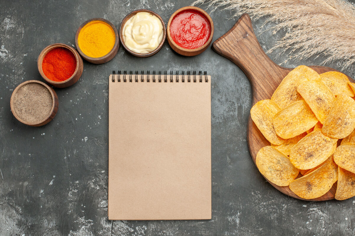 晚餐美味的薯片香料 番茄酱和笔记本在灰色背景上零食早餐盘子