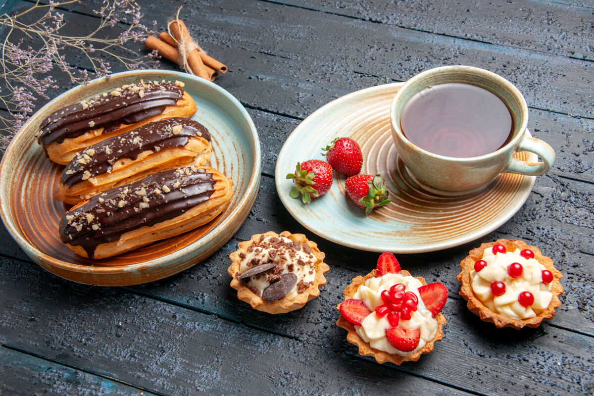 草莓下图：椭圆形盘子上放着巧克力 茶杯 茶托馅饼上放着草莓 深色木桌上放着肉桂美味底部食物