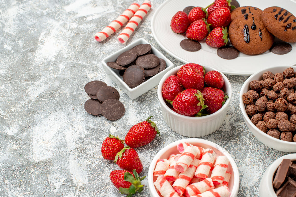 底部底部特写饼干草莓和圆形巧克力放在白色椭圆形盘碗上 糖果草莓巧克力谷类食品放在灰白色桌子的右侧 有自由空间右边碗巧克力