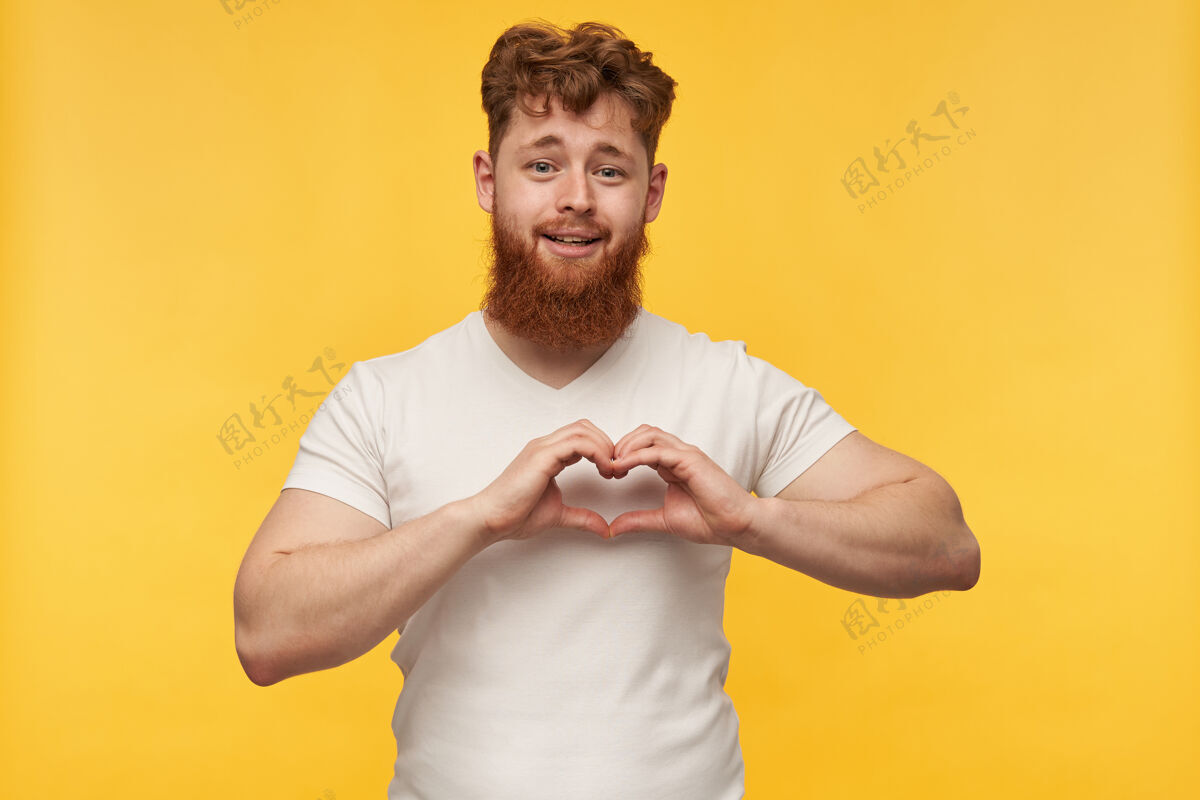 青春快乐的年轻人的肖像 穿着一件空白的t恤 用他的手臂展示着他的心 黄色的是爱的手势表情空白发型