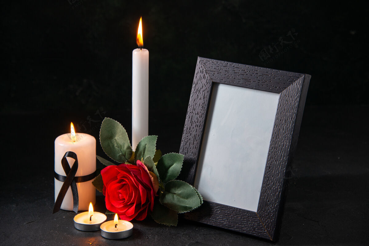 火焰前视图白色蜡烛与相框和花在黑暗的表面框架蜡烛葬礼
