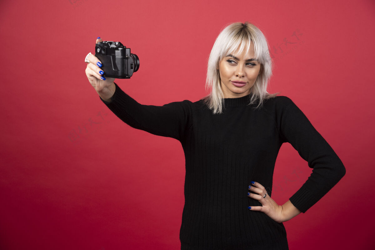 摄影师年轻女子用红色背景的照相机拍照高质量的照片拍摄时尚人