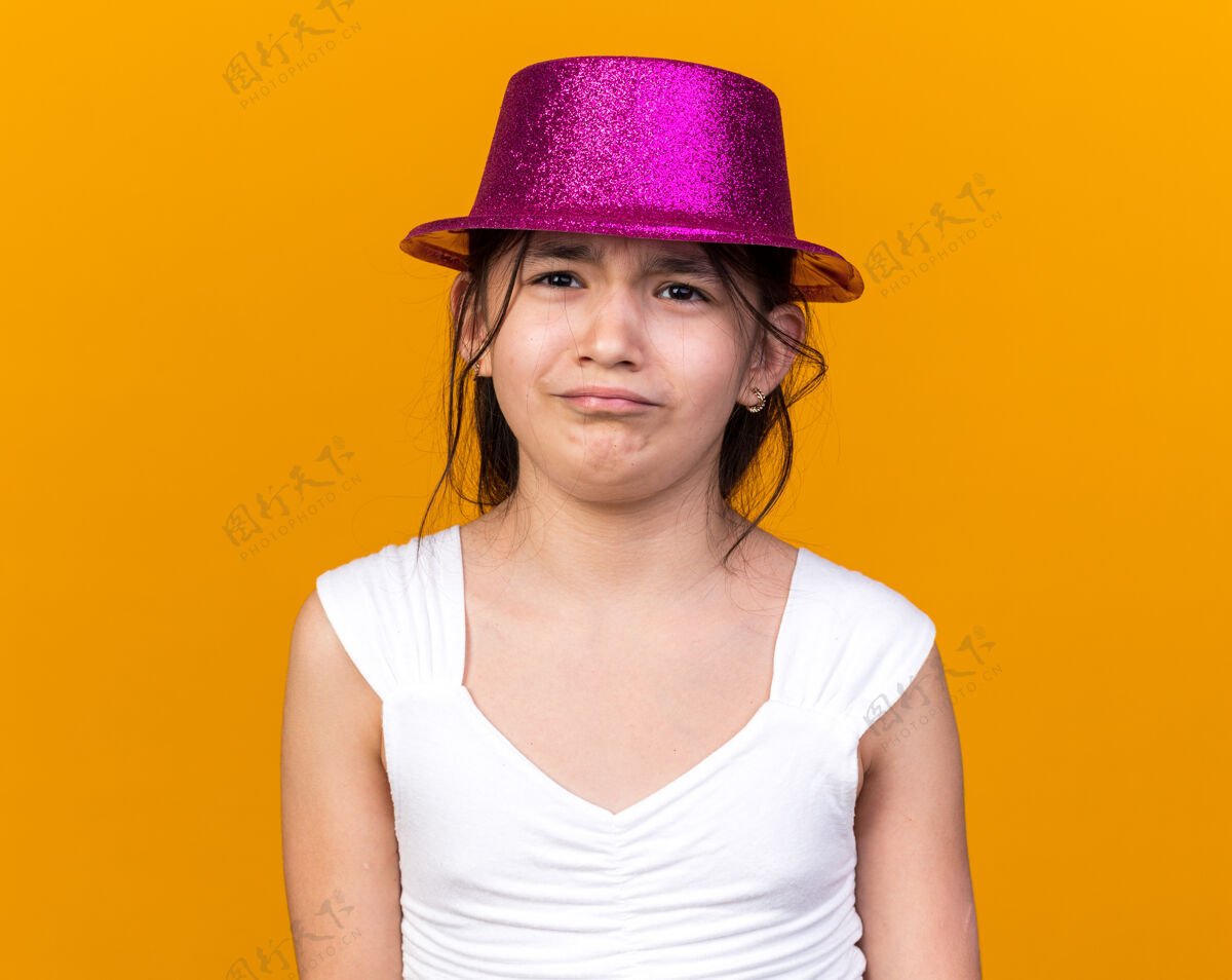 帽子悲伤的年轻白人女孩 戴着紫色派对帽 被隔离在橙色的墙上 留着复制空间女孩悲伤孤独