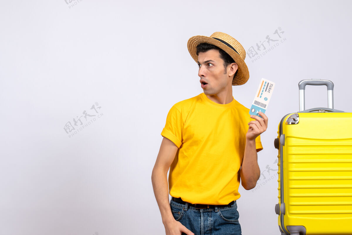 男正面图穿着黄色t恤的年轻游客站在黄色手提箱旁 拿着票看着左边票站立前面