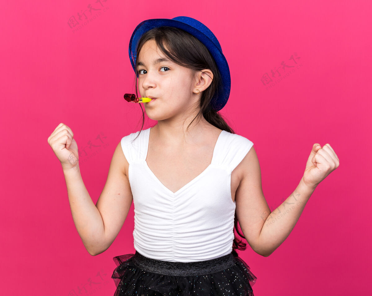 拳头高兴的年轻白人女孩与蓝色的党帽子吹党哨子 保持拳头在粉红色的墙上与复制空间隔离哨子年轻请保持