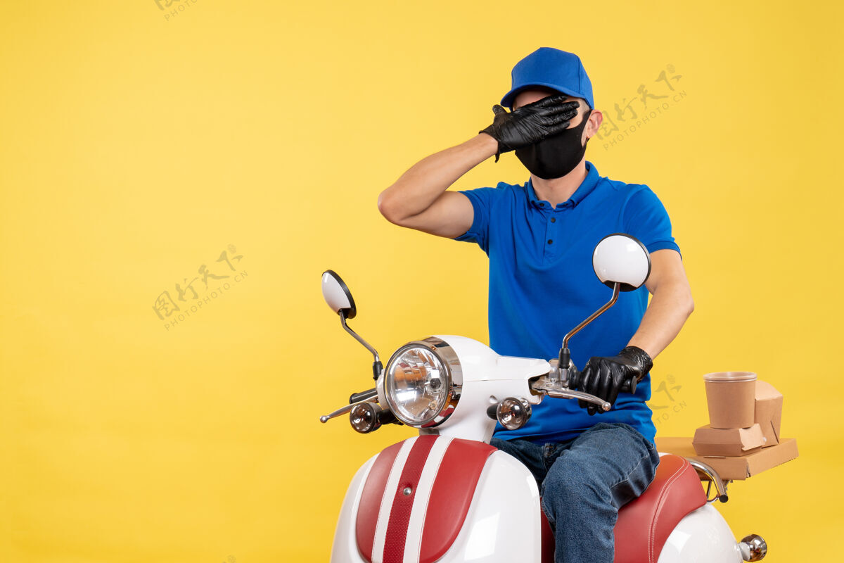 黄色正面图黄色背景上穿着蓝色制服的年轻男性信使-大流行服务工作病毒自行车工作摩托车病毒流行病