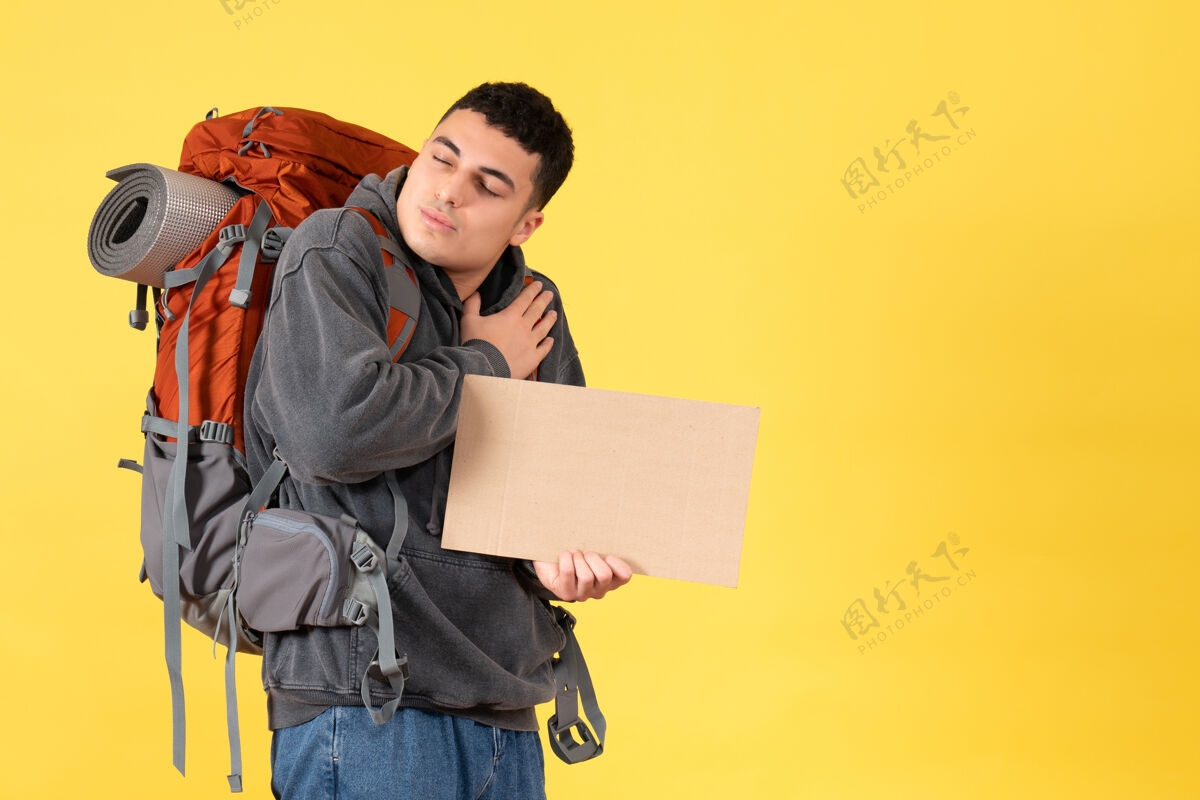 微笑前视图旅行者男子背着背包拿着纸板把手放在胸前抱着前面箱子