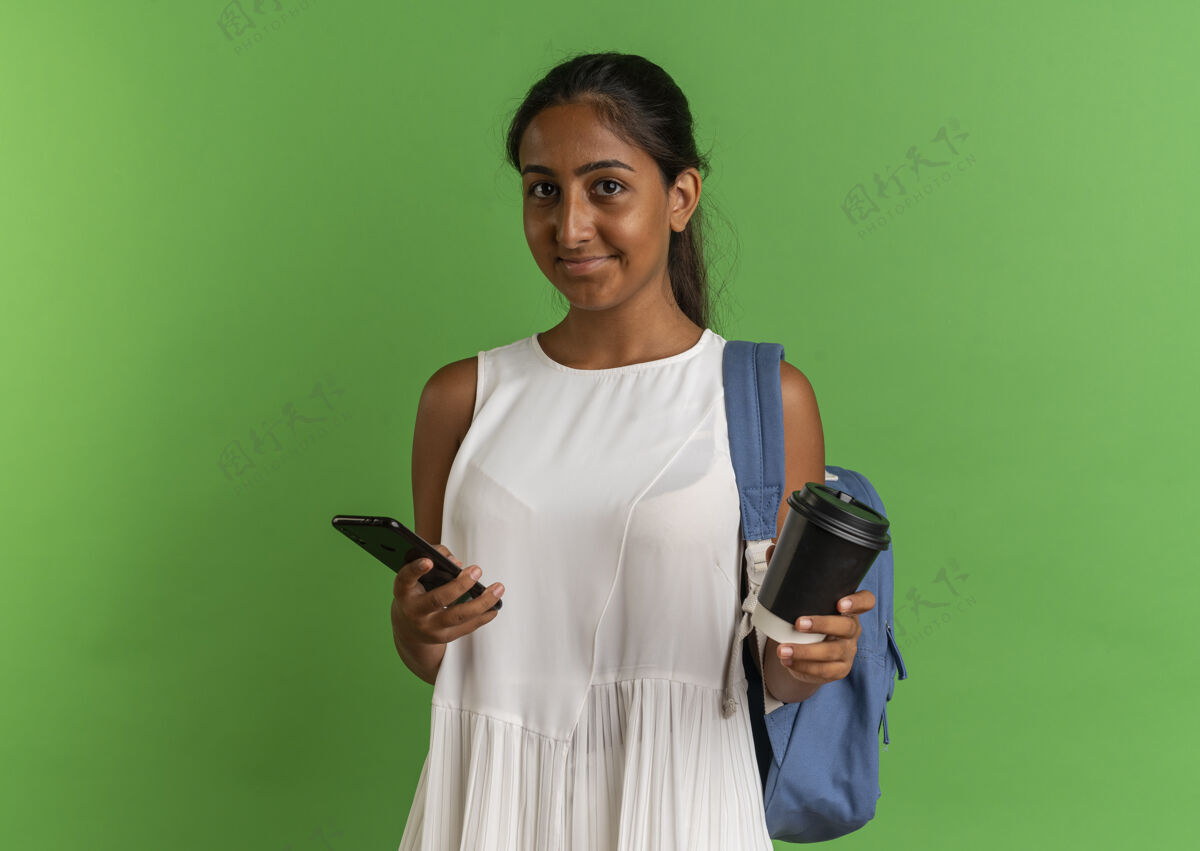 包高兴的年轻女学生穿着背袋举行咖啡杯和绿色背景的电话电话绿色年轻