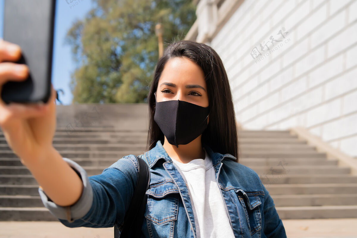 旅游年轻女子戴着口罩站在户外用手机自拍的照片聪明自我女人