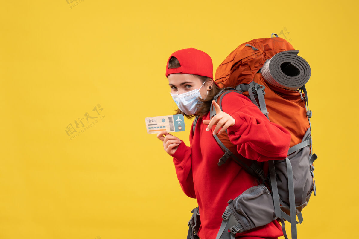 票正面图年轻的旅行女孩背着背包和面具拿着机票指着镜头工作帽子面具