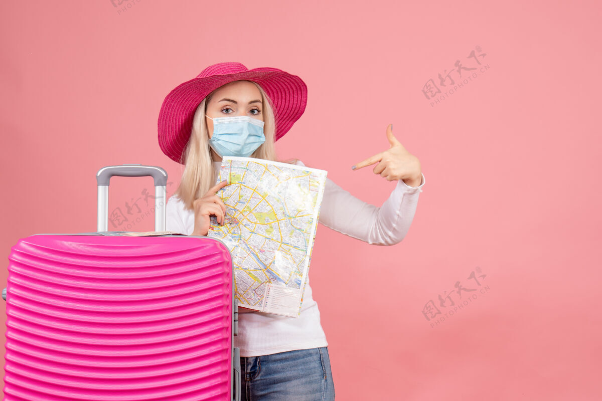 时尚前视图年轻女士站在手提箱旁指着地图帽子手提箱指