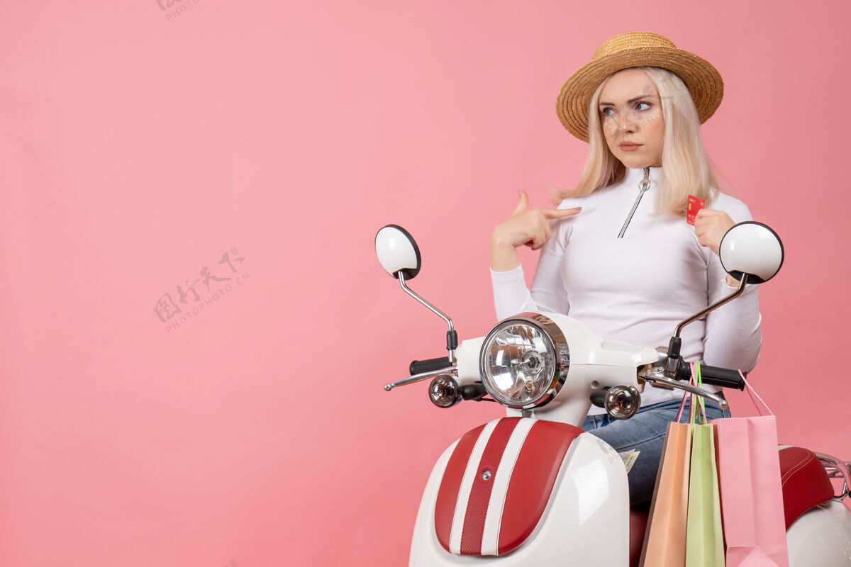 包正面图：骑着轻便摩托车的年轻女士 粉色墙上挂着购物袋前面摩托车摩托车