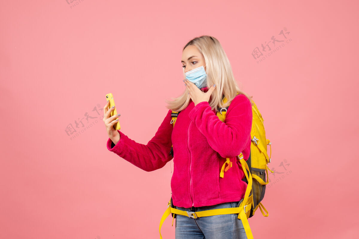 模特正面图：一位背着黄色背包 戴着口罩的女游客在用手机拍照拿快乐时尚