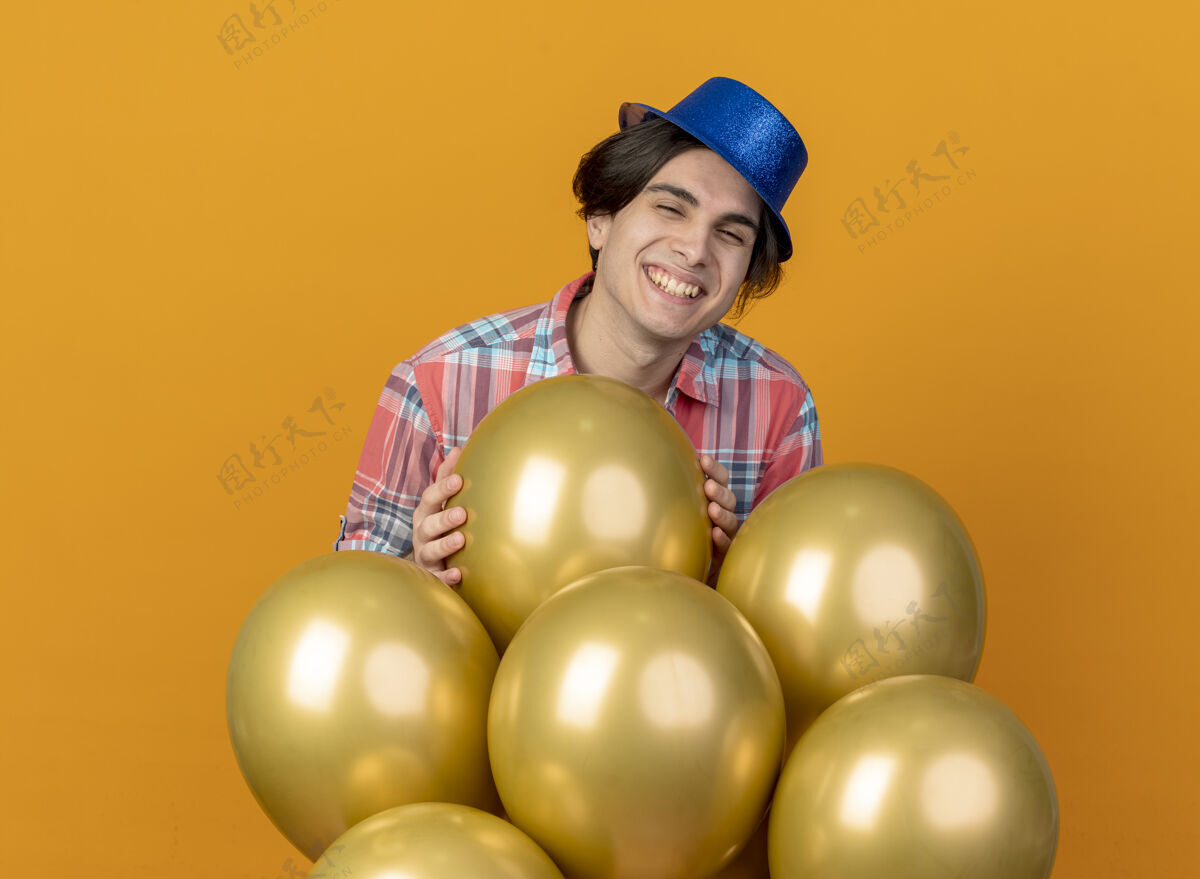 帽子微笑的帅哥戴着蓝色的派对帽 站在橙色的墙上 氦气球与世隔绝气球公民脸