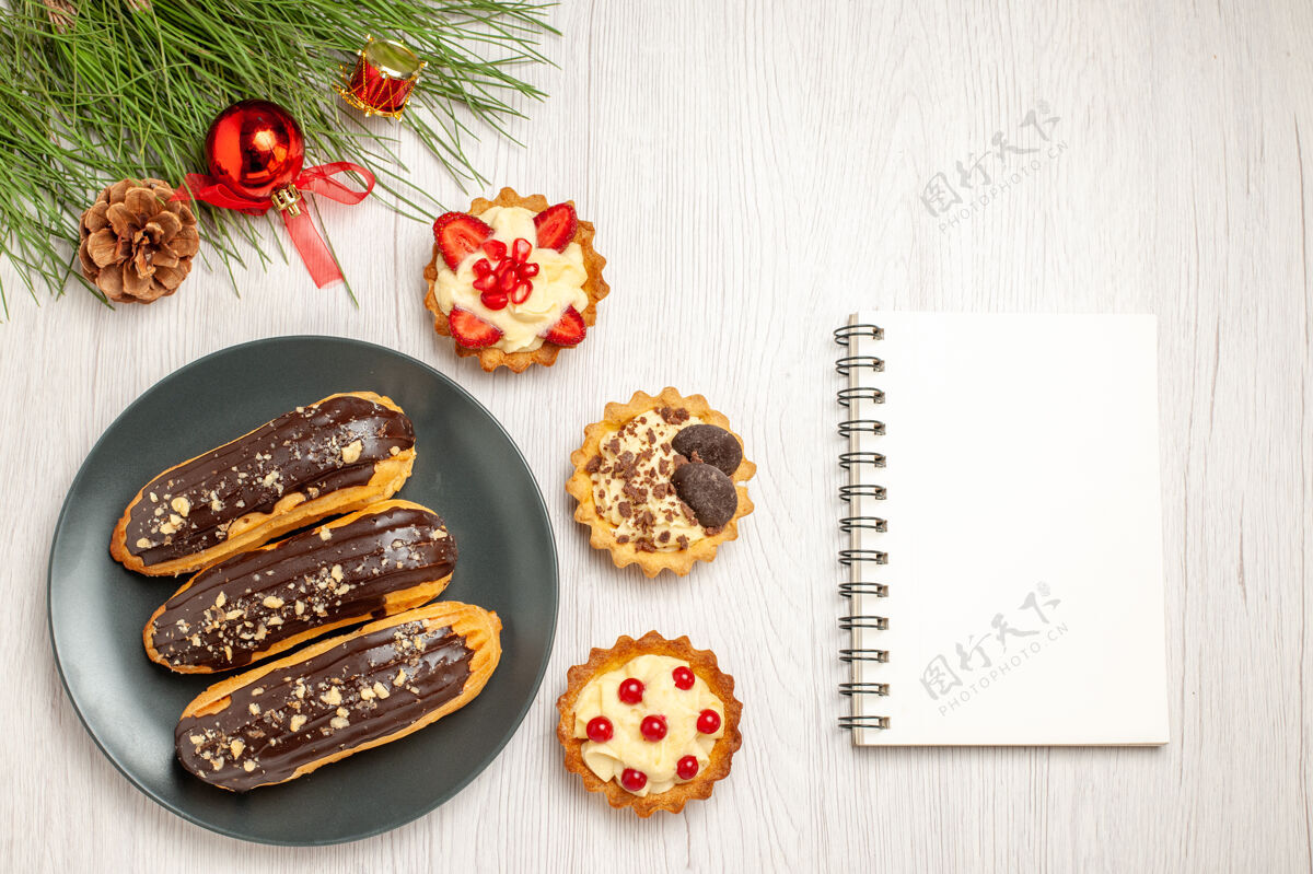 晚餐俯瞰图：灰色的馅饼和松树叶子上挂着巧克力蛋糕 左边是圣诞玩具 右边是白色的木质地面上的笔记本叶子松树玩具