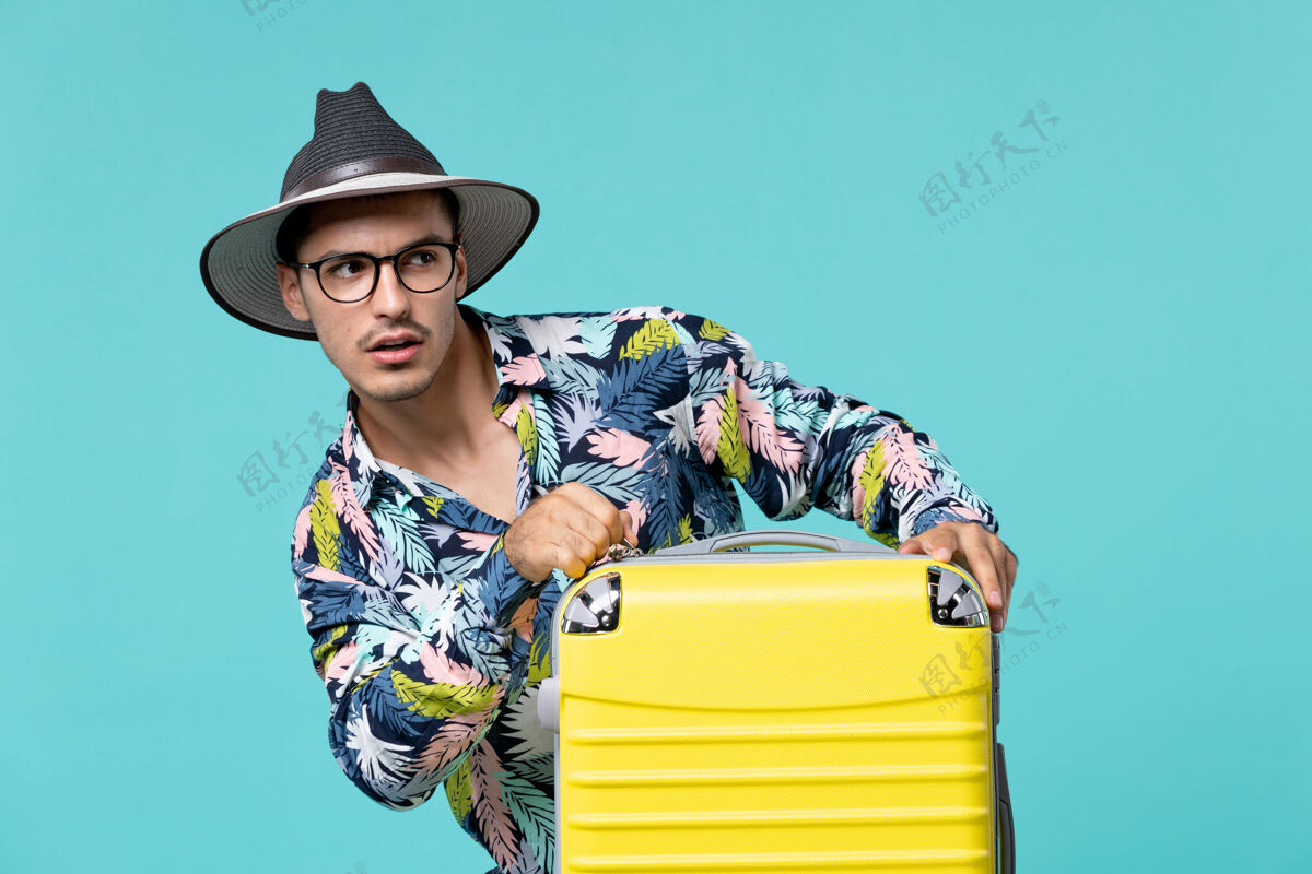 包年轻男子正拿着他的黄色袋子准备在蓝色的墙上旅行假期男性人