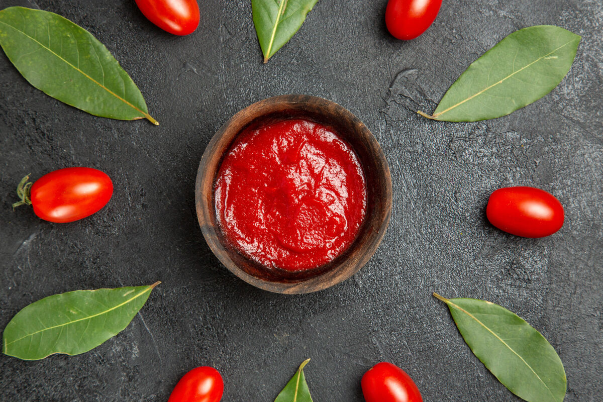 碗顶近距离观看一碗番茄酱围绕着樱桃番茄和月桂叶在黑暗的地面上健康新鲜水果