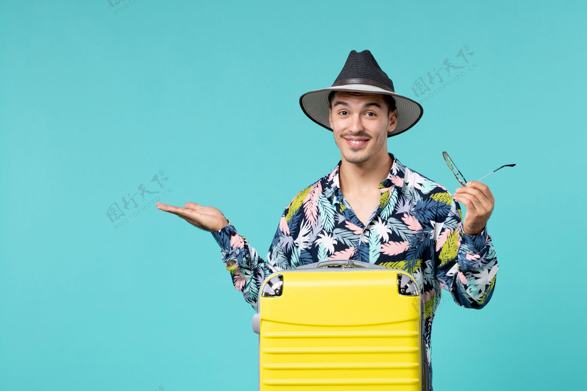 前面年轻男子正拿着他的黄包 准备在蓝色的墙上长途旅行度假旅行包