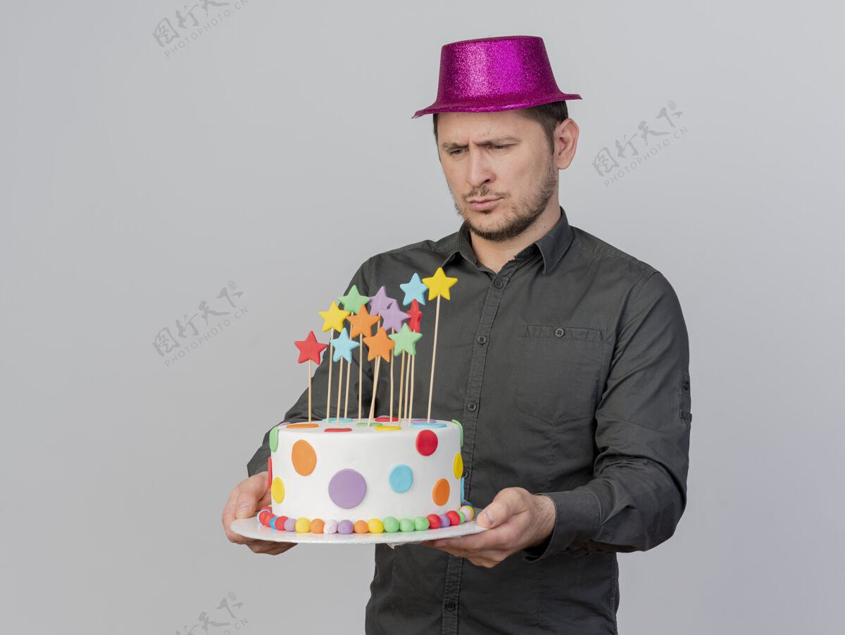 粉色给人印象深刻的年轻人戴着粉红色的帽子拿着蛋糕看着孤立的白色派对年轻人抱着