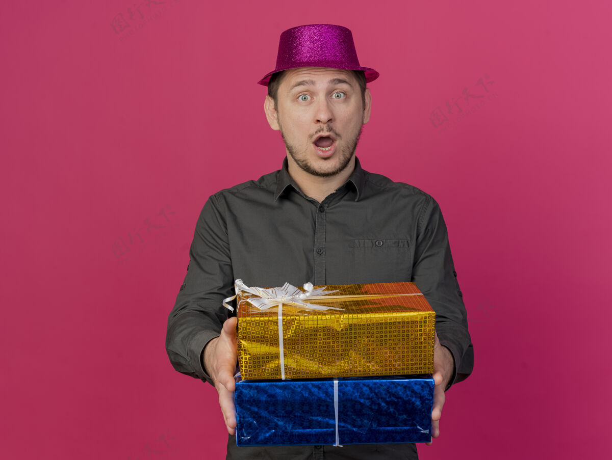 帽子惊讶的年轻人戴着粉红色的帽子拿着礼品盒孤立的粉红色派对礼物穿举行
