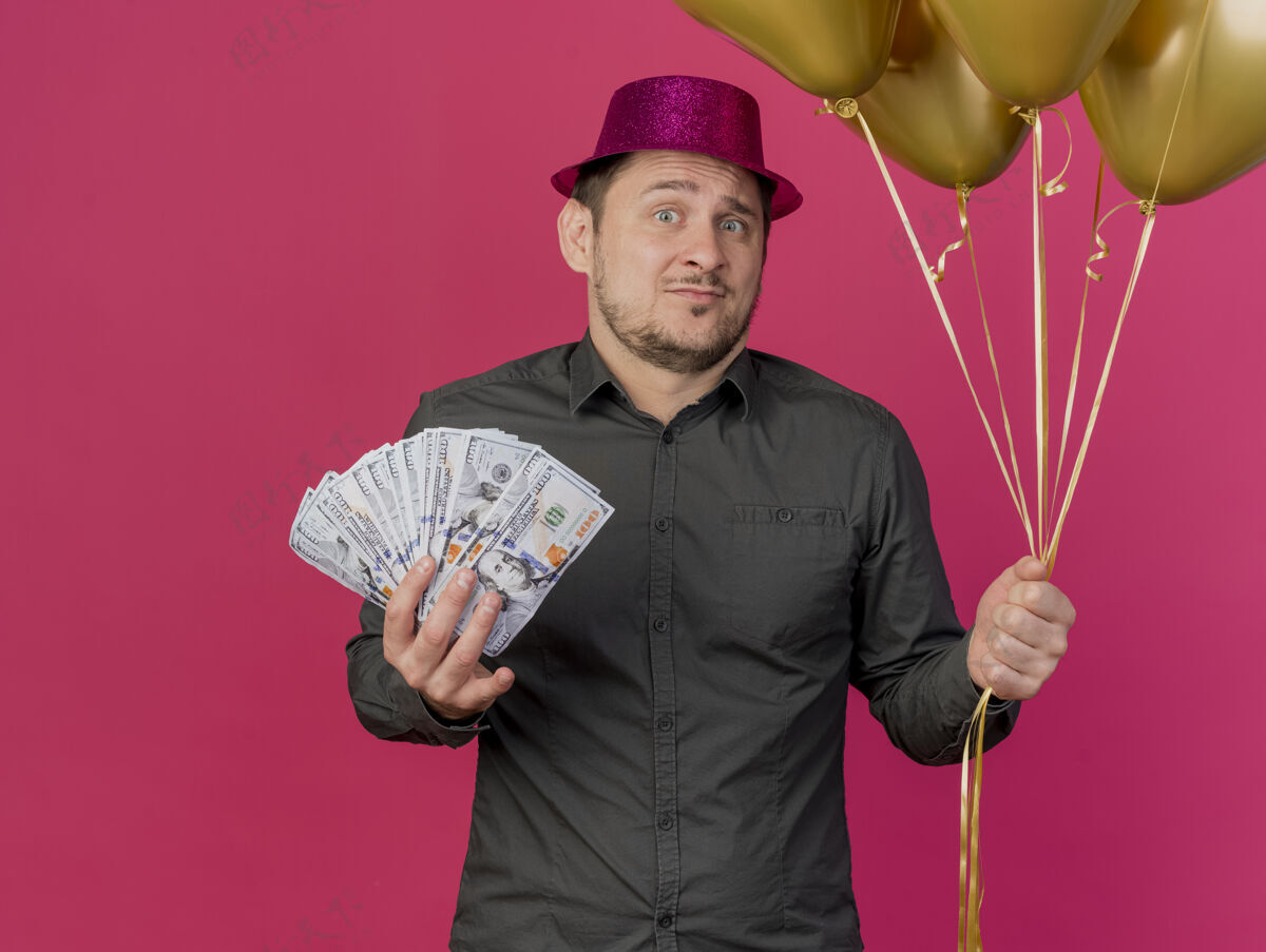 派对困惑的年轻人戴着粉红色的帽子拿着现金气球孤立在粉红色的聚会帽子粉色气球