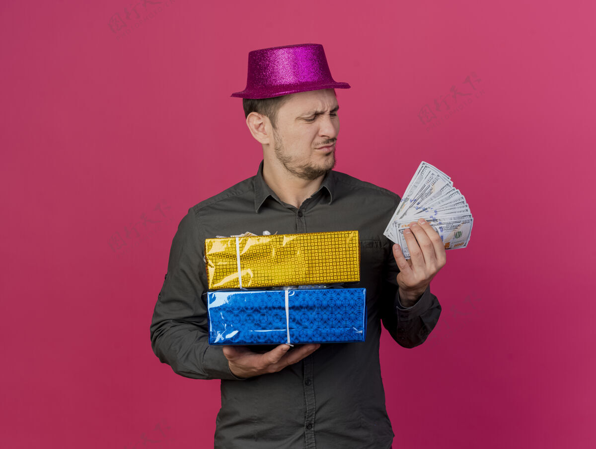 男人一个戴着粉红色帽子 拿着礼盒 看着手里的现金 孤零零地站在粉红色的桌子上的年轻人不愉快盒子帽子