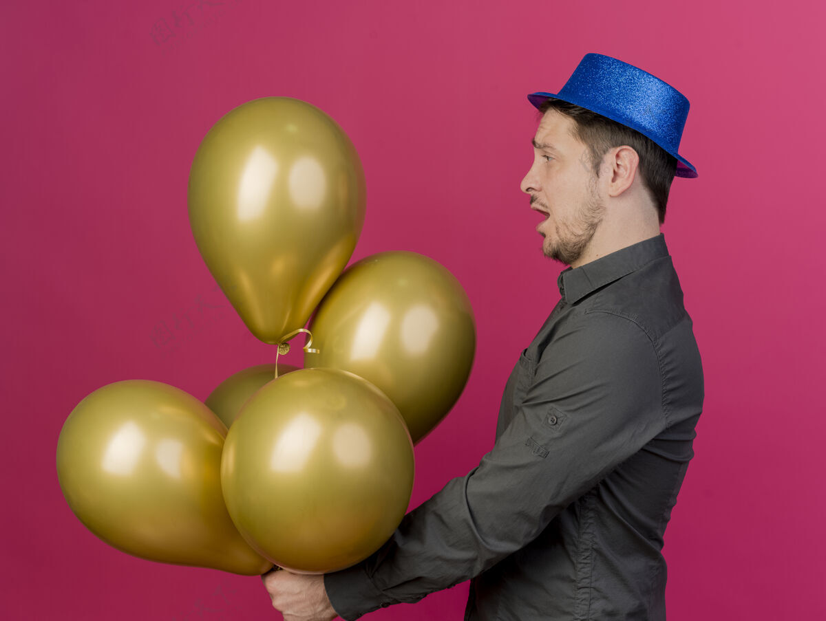 帽子令人印象深刻的年轻人戴着蓝色的帽子举行聚会 看着气球孤立的粉红色派对举行印象