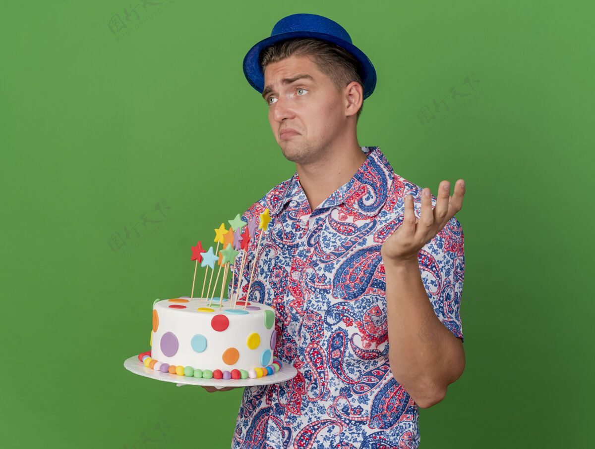 绿色迷茫的年轻人看着身边戴着蓝帽子拿着蛋糕摊开手孤立在绿色蛋糕抱着摊开