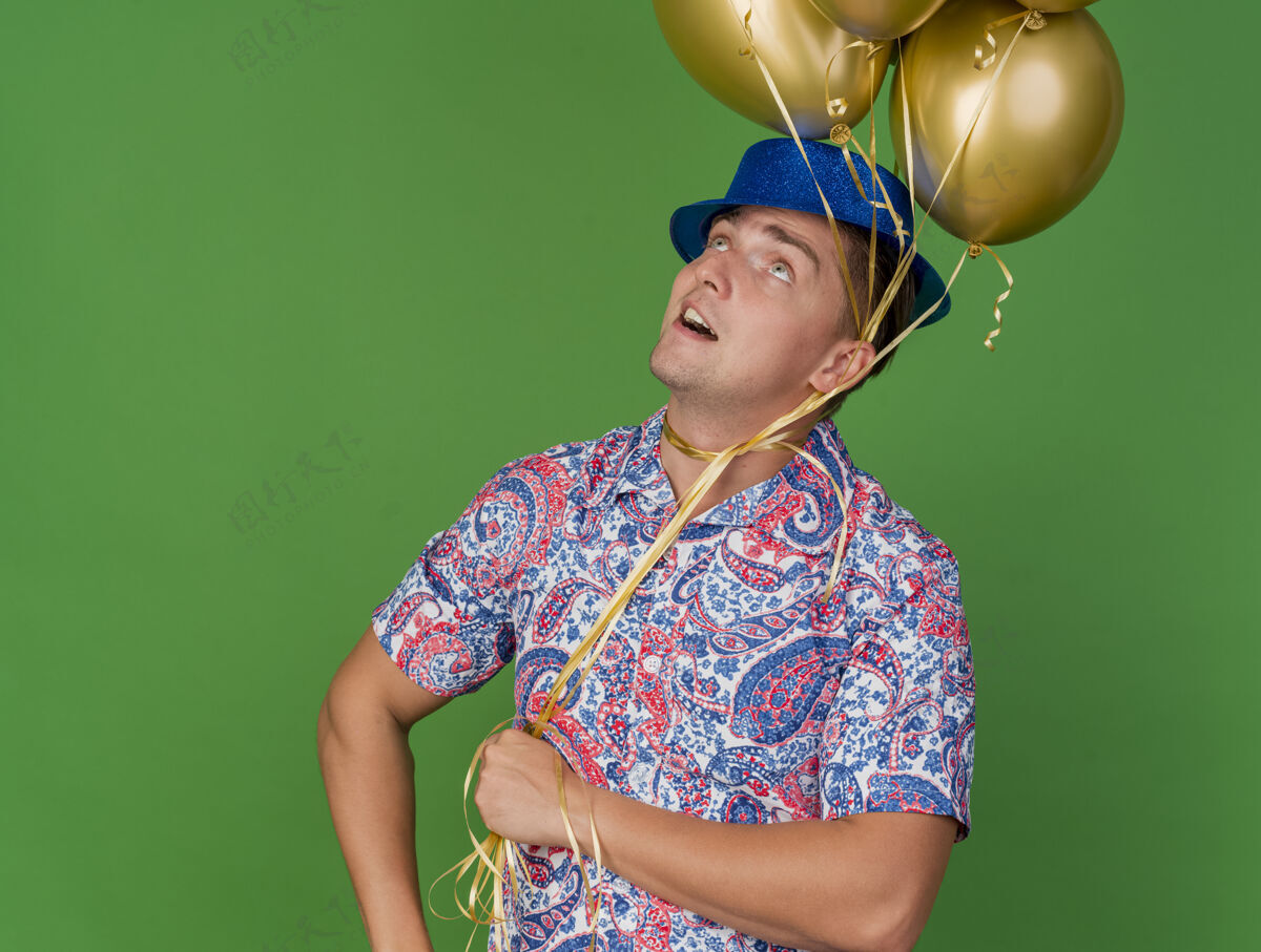 气球给人印象深刻的年轻人戴着蓝色帽子抬头看 脖子上围着气球孤立在绿色派对绿色年轻人