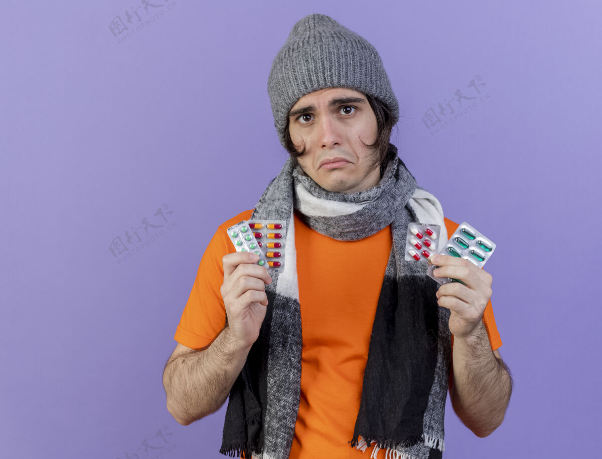 药丸悲伤的年轻人戴着冬天的帽子 戴着围巾 手里拿着紫色隔离的药丸围巾紫色男人