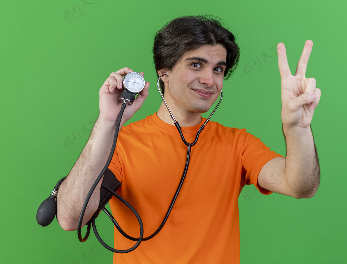 男人高兴的年轻人戴着听诊器拿着血压计显示和平姿态隔离在绿色戴疾病血压计