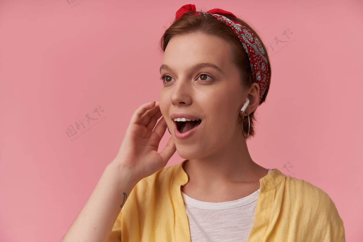 手自然妆容的女人穿着白色t恤 黄色衬衫和红色头巾 一边看一边惊讶地微笑在粉红色的墙上魅力姿势粉色