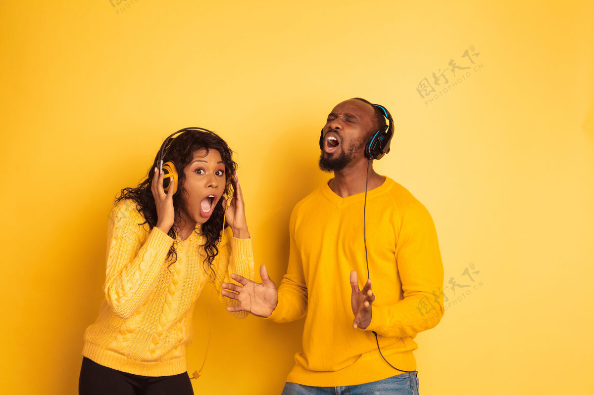 明亮年轻感性的非裔美国人 穿着鲜艳的休闲服 在黄色背景上摆姿势美丽的情侣人类情感的概念 面部表情 广告听音乐时震惊金融成人化妆品