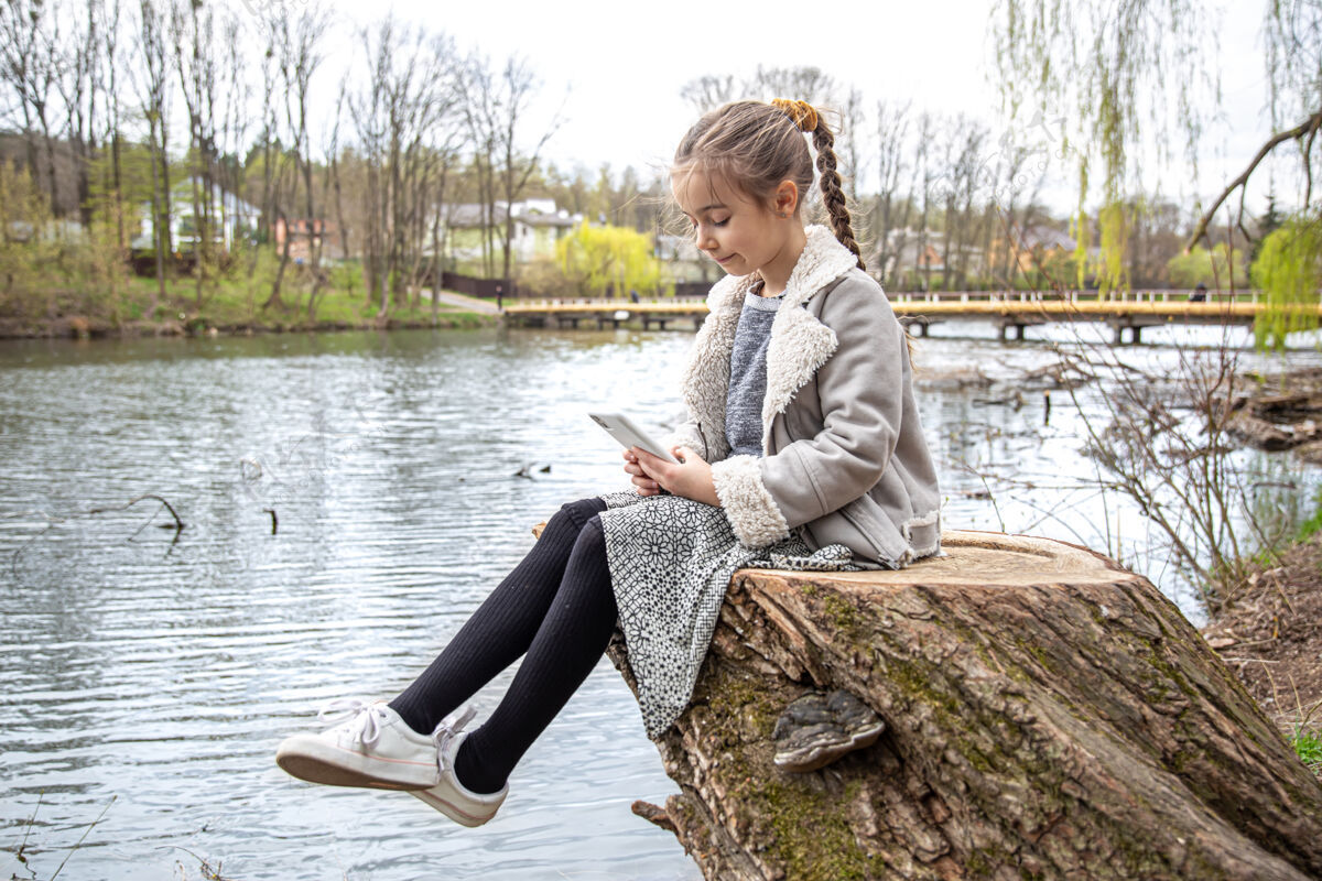 道路一个小女孩坐在河边看手机 不注意周围的自然环境互联网在线童年