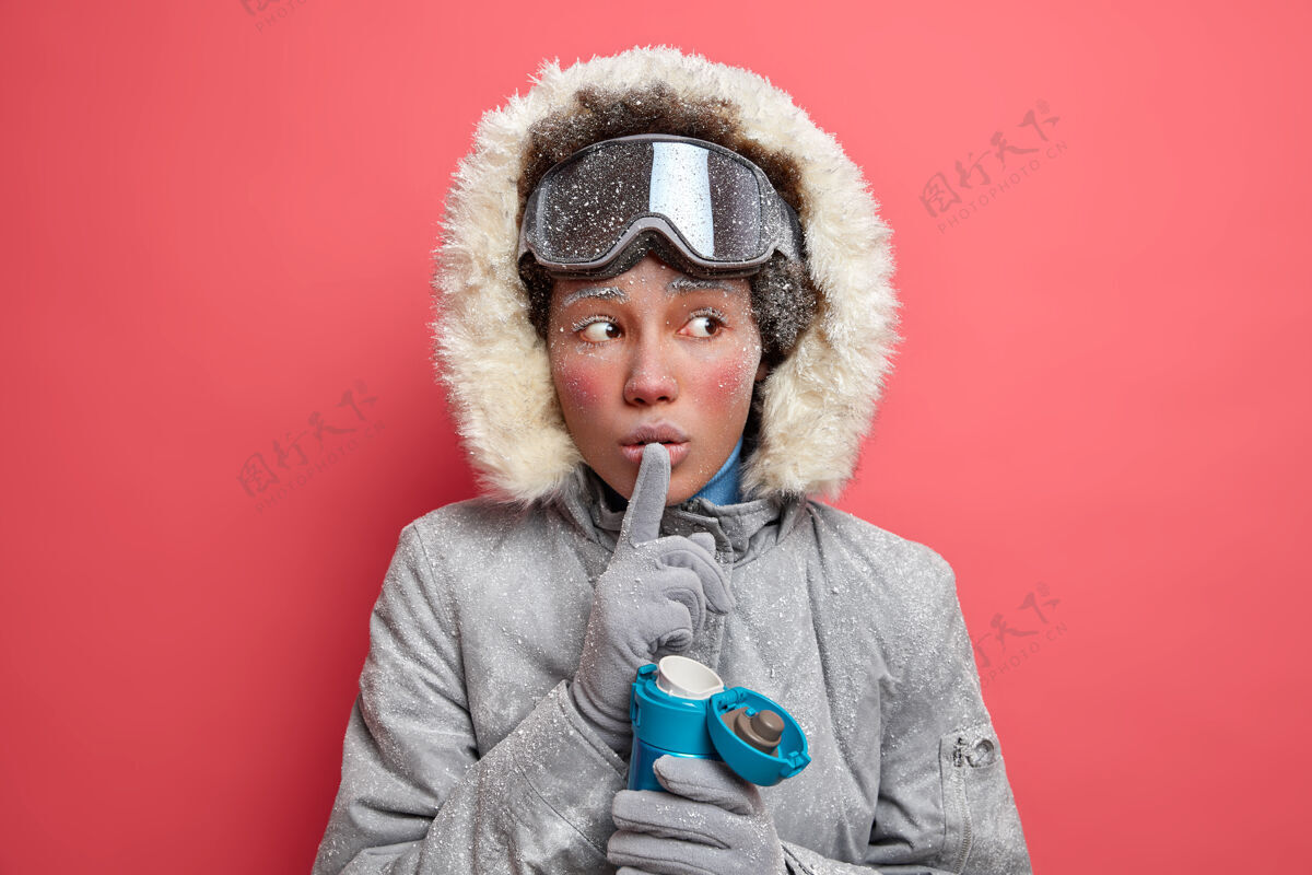 冬天神秘活跃的女人做了一个沉默的手势 告诉她秘密的目光移开了 试图用热饮料取暖 她穿着冬天的外套 有着一张红色冰冷的脸冰室内保温瓶