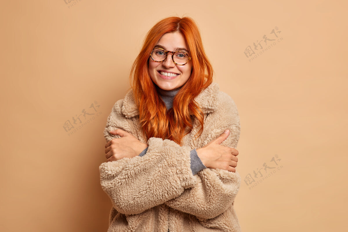 年轻年轻快乐的姜黄色年轻白种女人 穿着舒适的皮衣 拥抱自己 感受温暖 享受她的寒假搞笑乐观温暖
