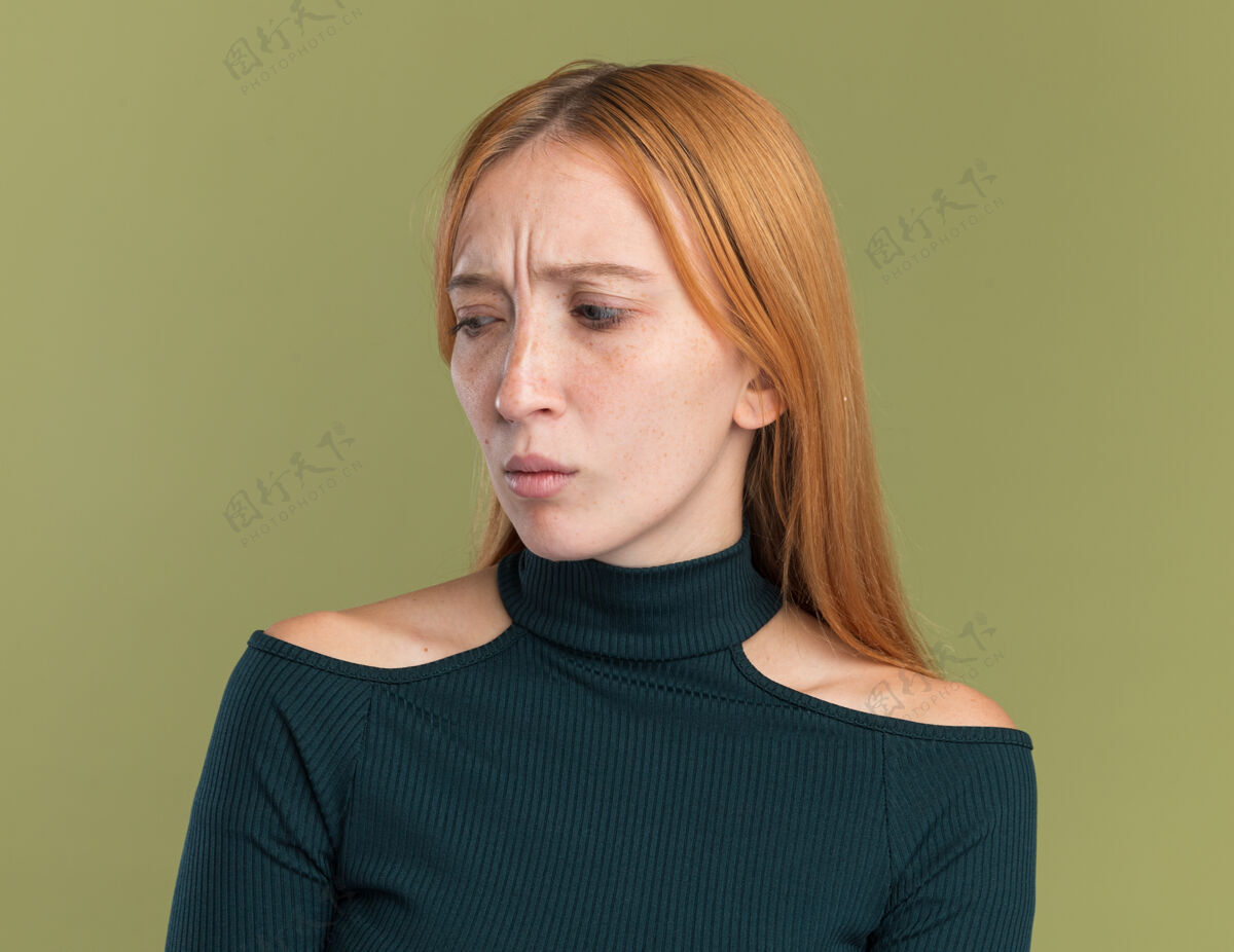 年轻笨手笨脚的年轻红发姜女 长着雀斑 一边看着橄榄绿雀斑壁板不知所措