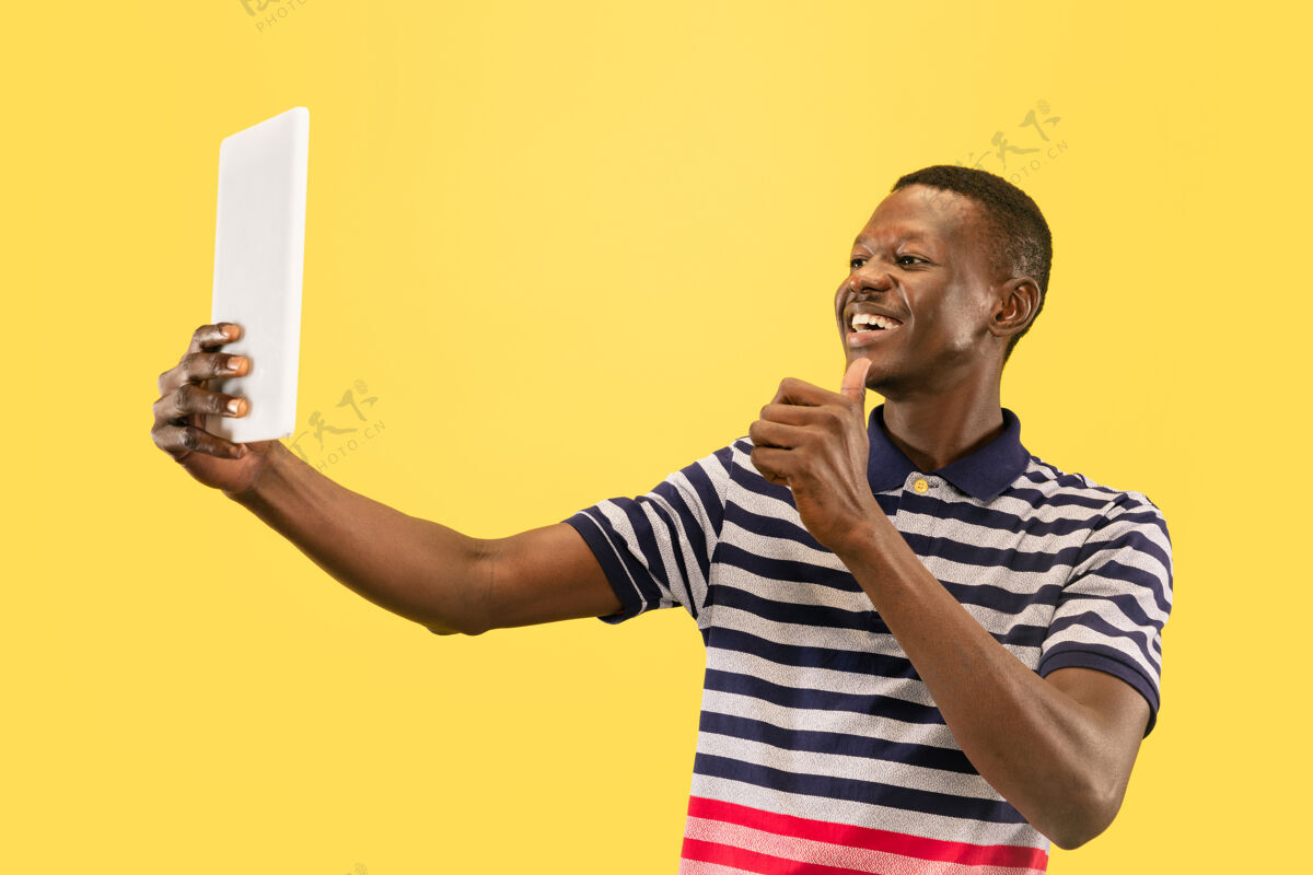 男孩快乐的非洲裔美籍年轻男子 以平板电脑隔离在黄色工作室背景下 面部表情美丽的男性半身肖像人类情感的概念 面部表情美国人学生漂亮