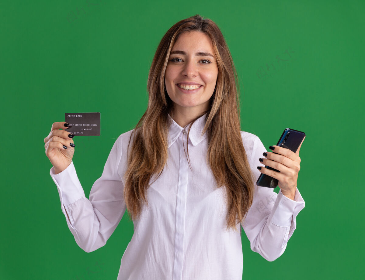 电话年轻漂亮的高加索女孩微笑着拿着信用卡和手机在绿色年轻漂亮信用
