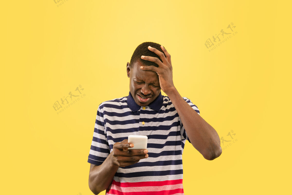 商人年轻的非洲裔美国男子用智能手机隔离在黄色的工作室背景下 面部表情美丽的男性半身肖像人类情感的概念 面部表情非洲人成功幸运