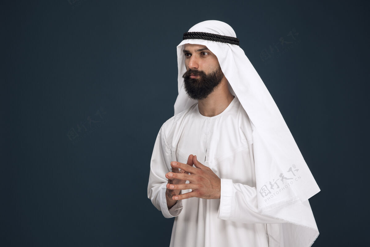 文化深蓝色工作室背景上的半身阿拉伯沙特商人肖像年轻的男模站着 看起来很体贴商业 金融 面部表情 人类情感的概念惊奇东方东方