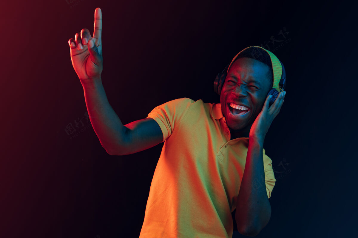 头年轻帅气快乐的时髦男人在霓虹灯下用耳机在黑工作室听音乐迪斯科舞厅 夜总会 嘻哈风格 积极的情绪 面部表情 舞蹈概念球迷哥斯达黎加人
